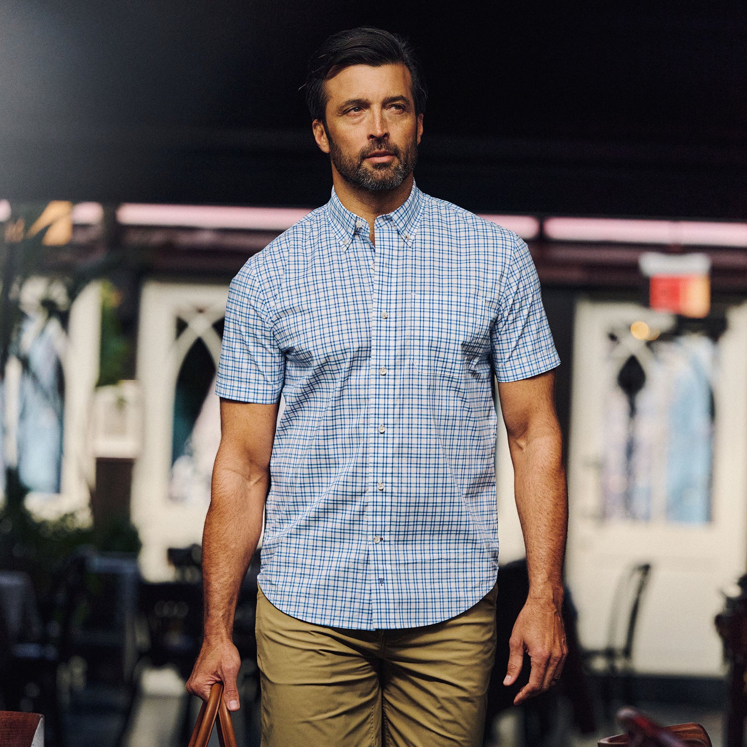 Man wears Tom Beckbe Powell Performance Shirt (Short Sleeve) and khaki pants outdoors, holding a brown bag.