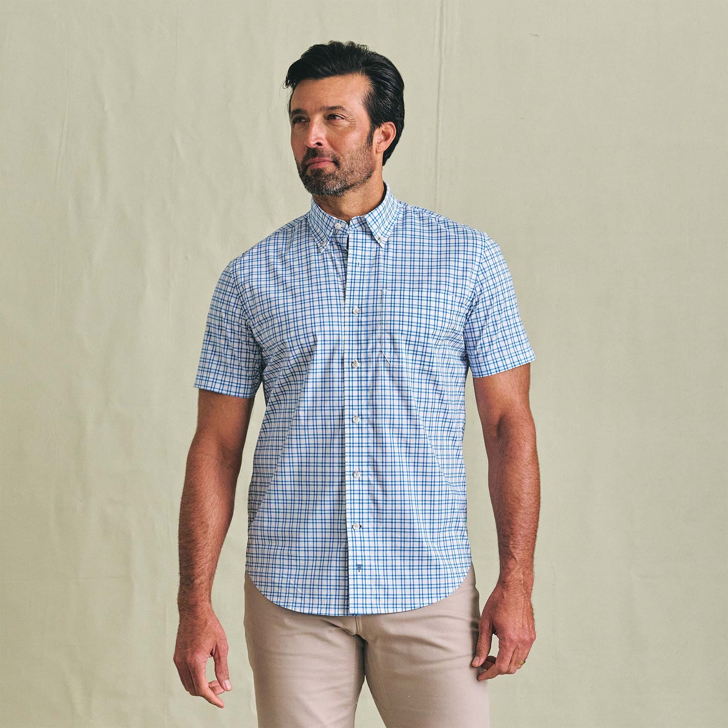 Man in Tom Beckbe Powell Performance Shirt (Short Sleeve), blue plaid, and beige pants against a plain light background.