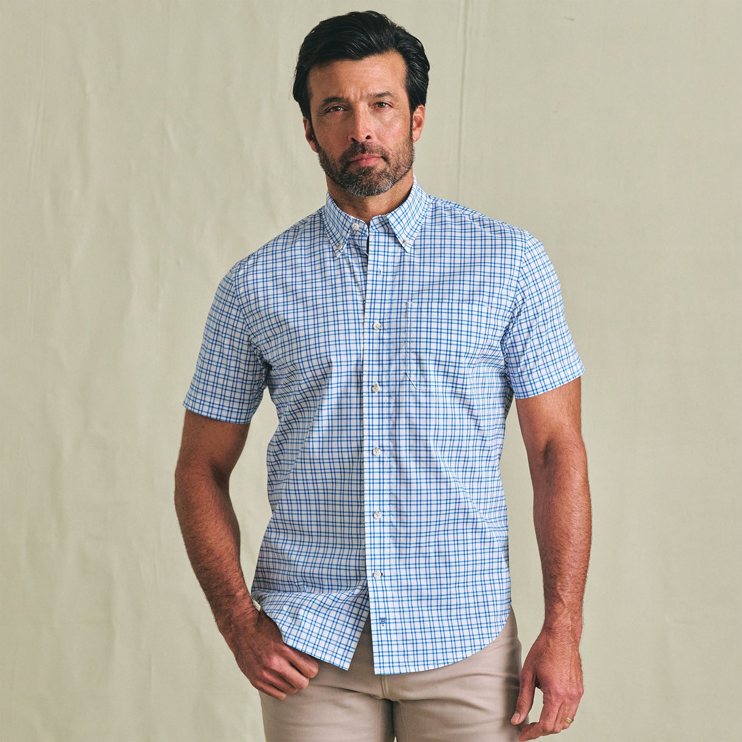 Man wears the Tom Beckbe Powell Performance Shirt (Short Sleeve) in blue and white checks with beige pants.