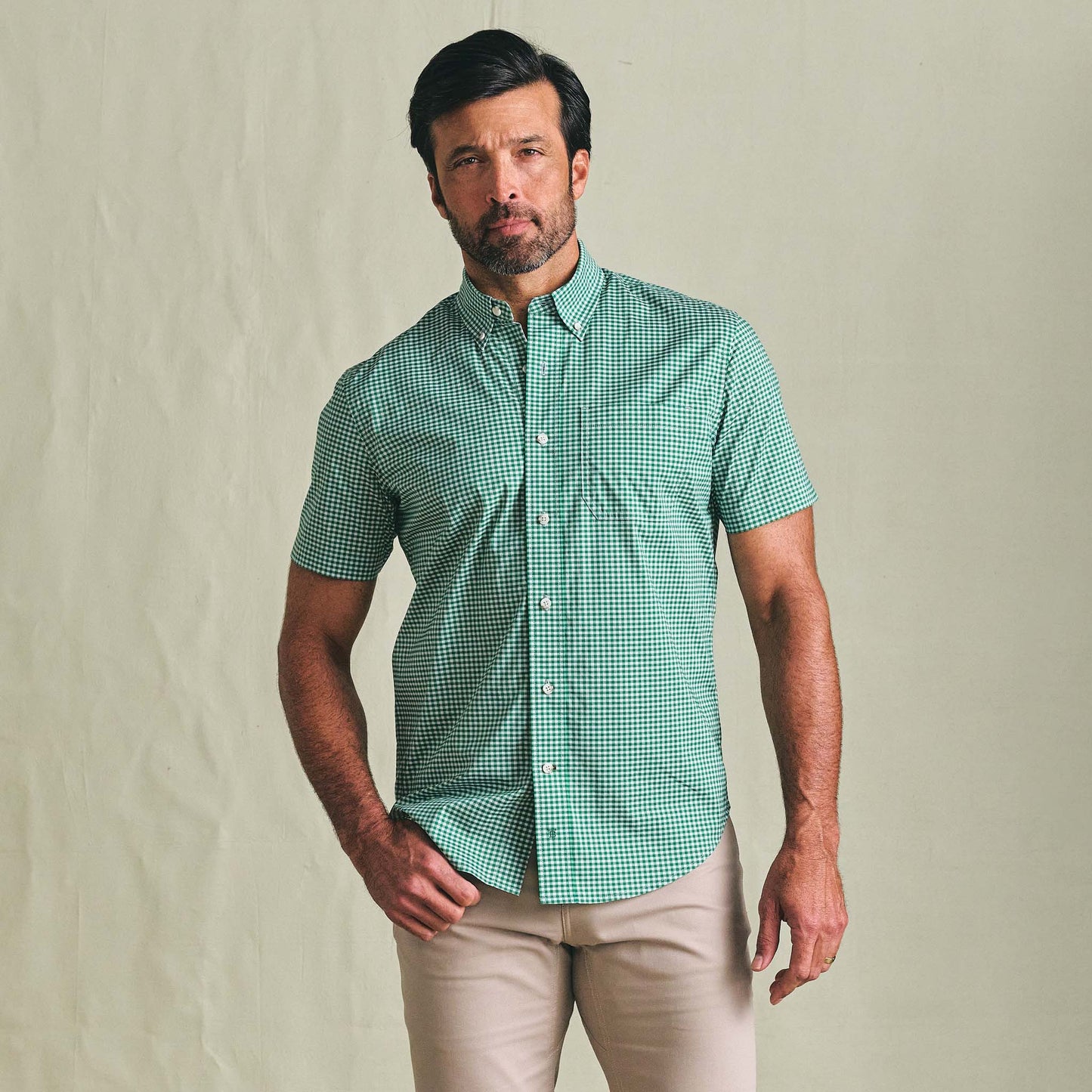 Man wears Tom Beckbe Powell Performance SS Shirt in green check, beige pants, against a light background.