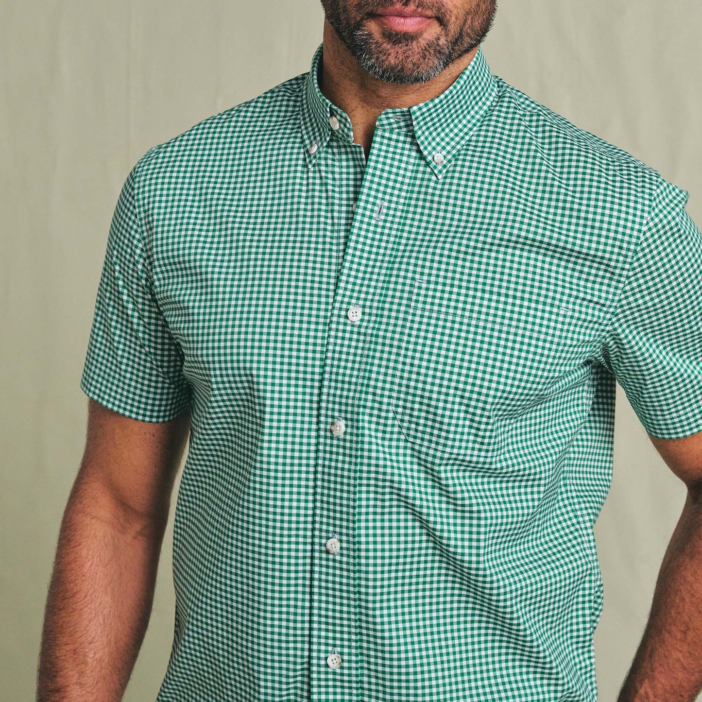 A man wears the Tom Beckbe Powell Performance Shirt, short sleeve, UPF 30+, green and white checks, plain background.
