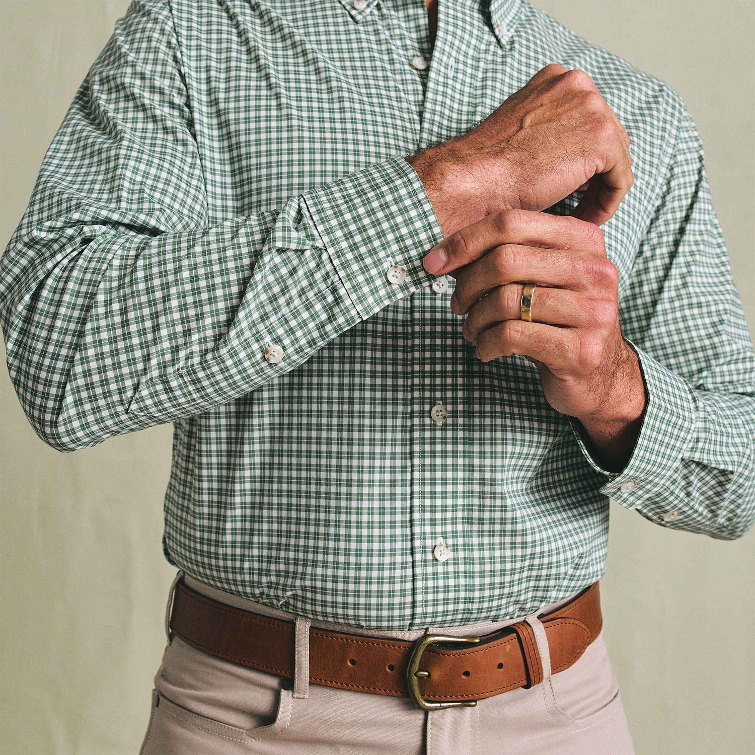 Person in a Tom Beckbe Powell Performance Shirt (green check, UPF 30+), beige pants, and brown belt adjusting a sleeve.