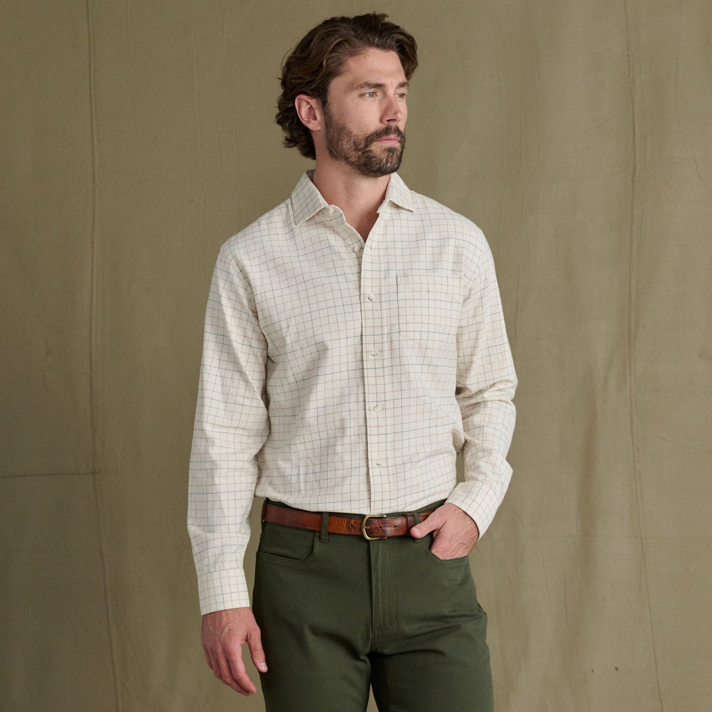 Man wearing a Tom Beckbe Prescott Estate Twill Shirt and olive green pants stands before a plain brown background.