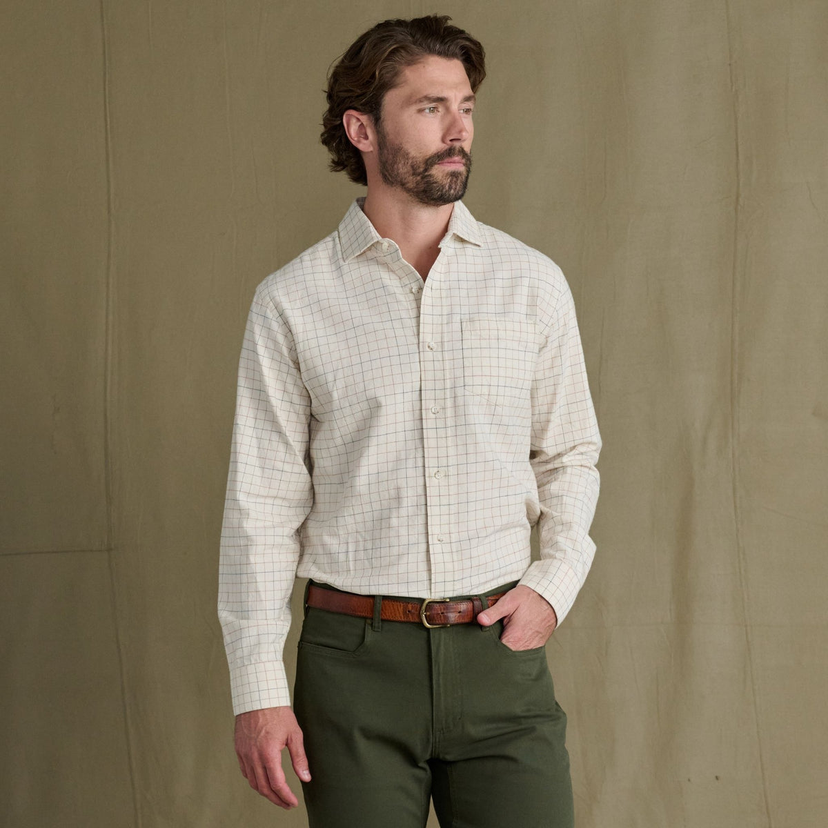 Man wearing a Tom Beckbe Prescott Estate Twill Shirt and olive green pants stands before a plain brown background.
