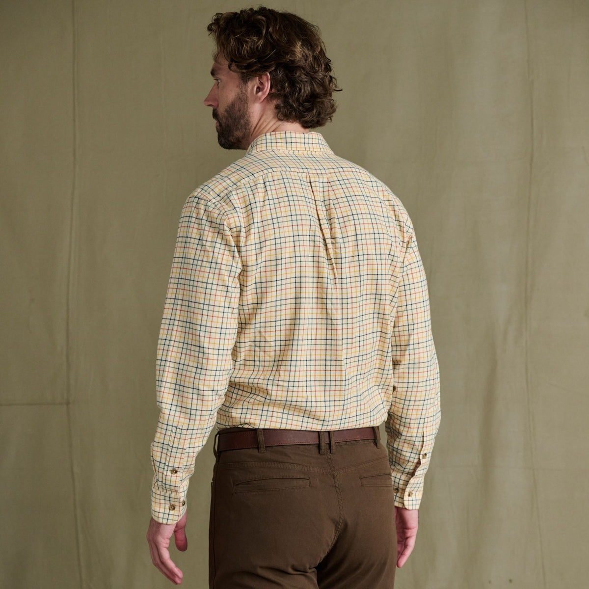 Man facing away wears a Tom Beckbe Prescott Estate Twill Shirt and brown pants, in front of a beige background.