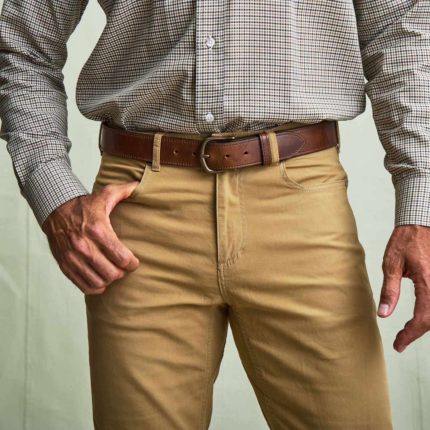 A man in a checked shirt and Tom Beckbe's Reid Straight Leg Cotton Chino Pant stands with one hand in his pocket.