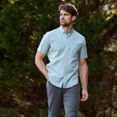 A man in a light green shirt wears Tom Beckbe Reid Straight Leg Cotton Chino Pants outdoors with trees behind him.