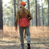 Man in orange cap and brown shirt walks through forest wearing a Tom Beckbe Strap Vest.