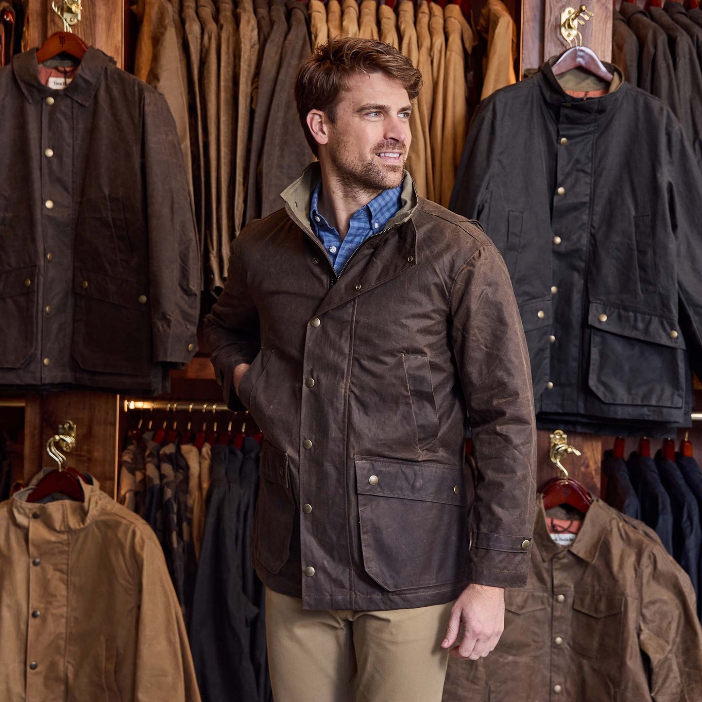 A man in a brown Tom Beckbe Tensaw Jacket stands in a store among racks of durable shelter cloth jackets.
