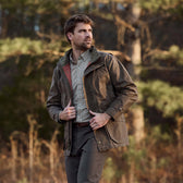 A man in a Tom Beckbe Tensaw Jacket stands outside in a forest.