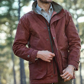 A person in a Fox Red Tensaw Jacket by Tom Beckbe over a checkered shirt, outdoors among trees, resembling Wildrose Kennels.
