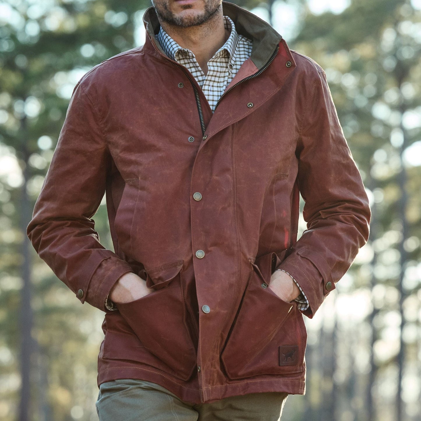 A man in a Tom Beckbe Fox Red Tensaw Jacket stands outdoors with hands in pockets, trees backdrop.