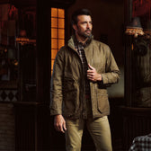 Man wears a brown Tom Beckbe Tensaw Jacket and khaki pants, standing indoors with one hand on his durable jacket.