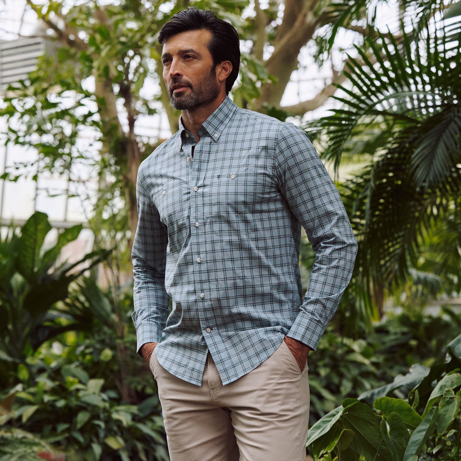 Man in a greenhouse wearing the Tom Beckbe Tidewater Shirt and beige pants, hands in his pockets.