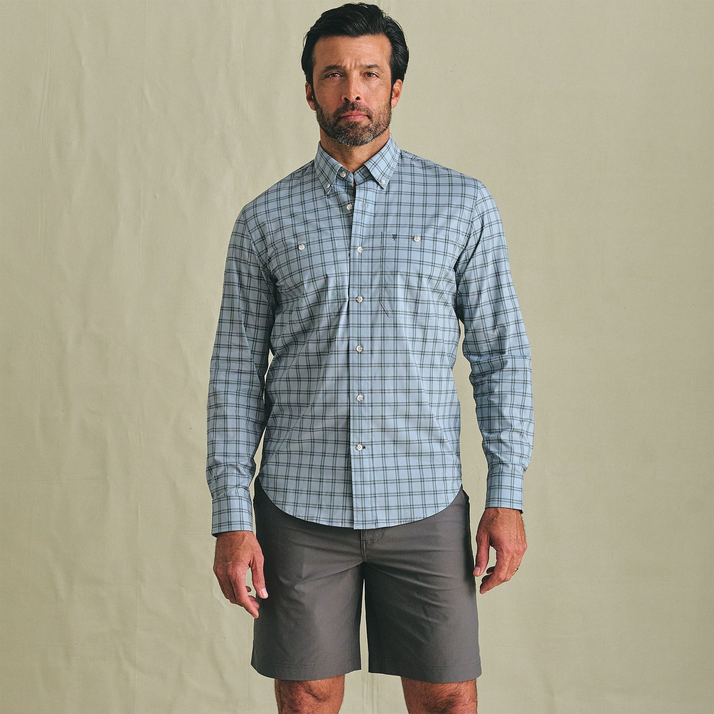 A man wears the Tom Beckbe Tidewater Shirt and gray shorts, standing against a plain beige background.