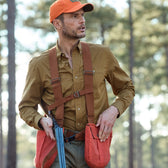 Man in a Tom Beckbe brown Tidewater Shirt with UPF 30+ holds a double-barreled shotgun, trees in the background.