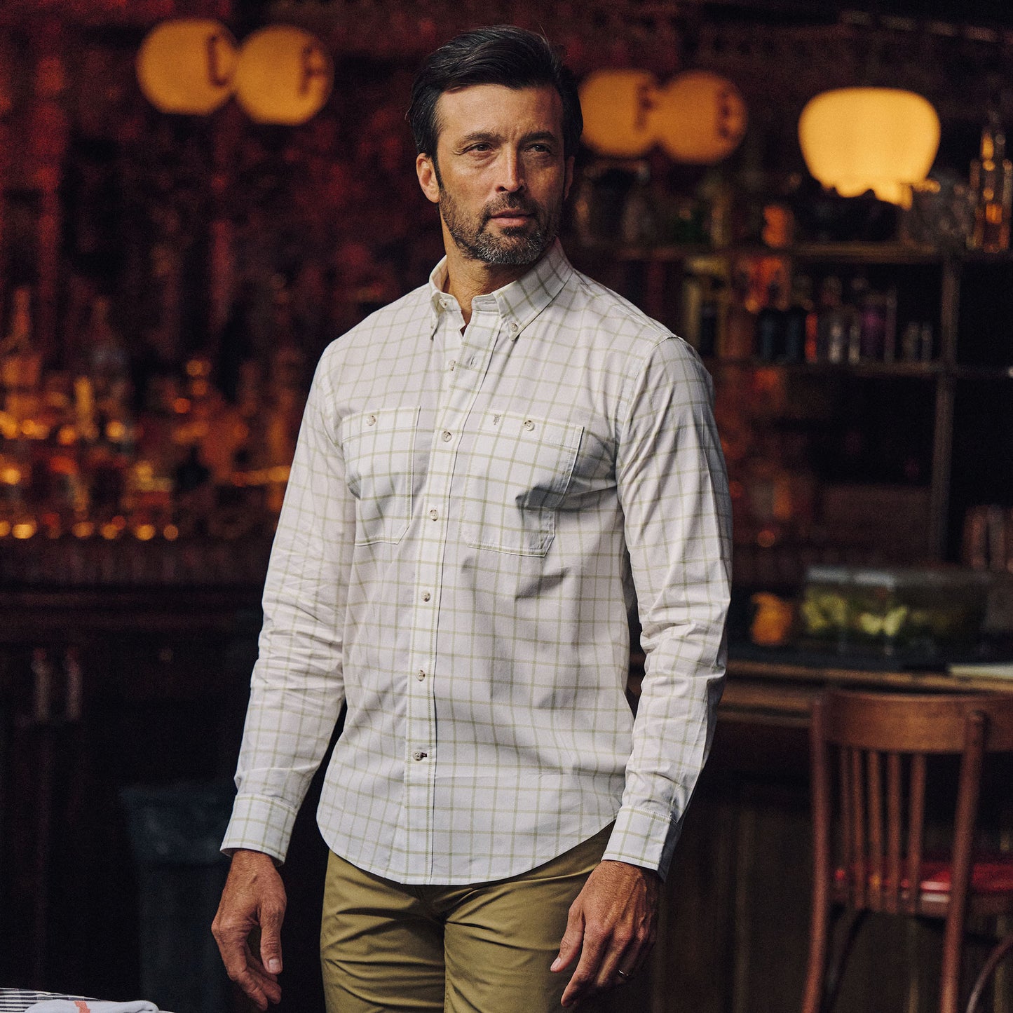 Man wears the Tom Beckbe Tidewater Shirt indoors, standing among wooden furniture in a dimly lit room.