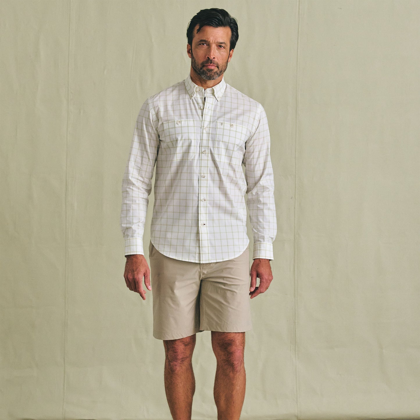 Man facing forward in a Tom Beckbe Tidewater Shirt, UPF 30+, and beige shorts against a plain backdrop.