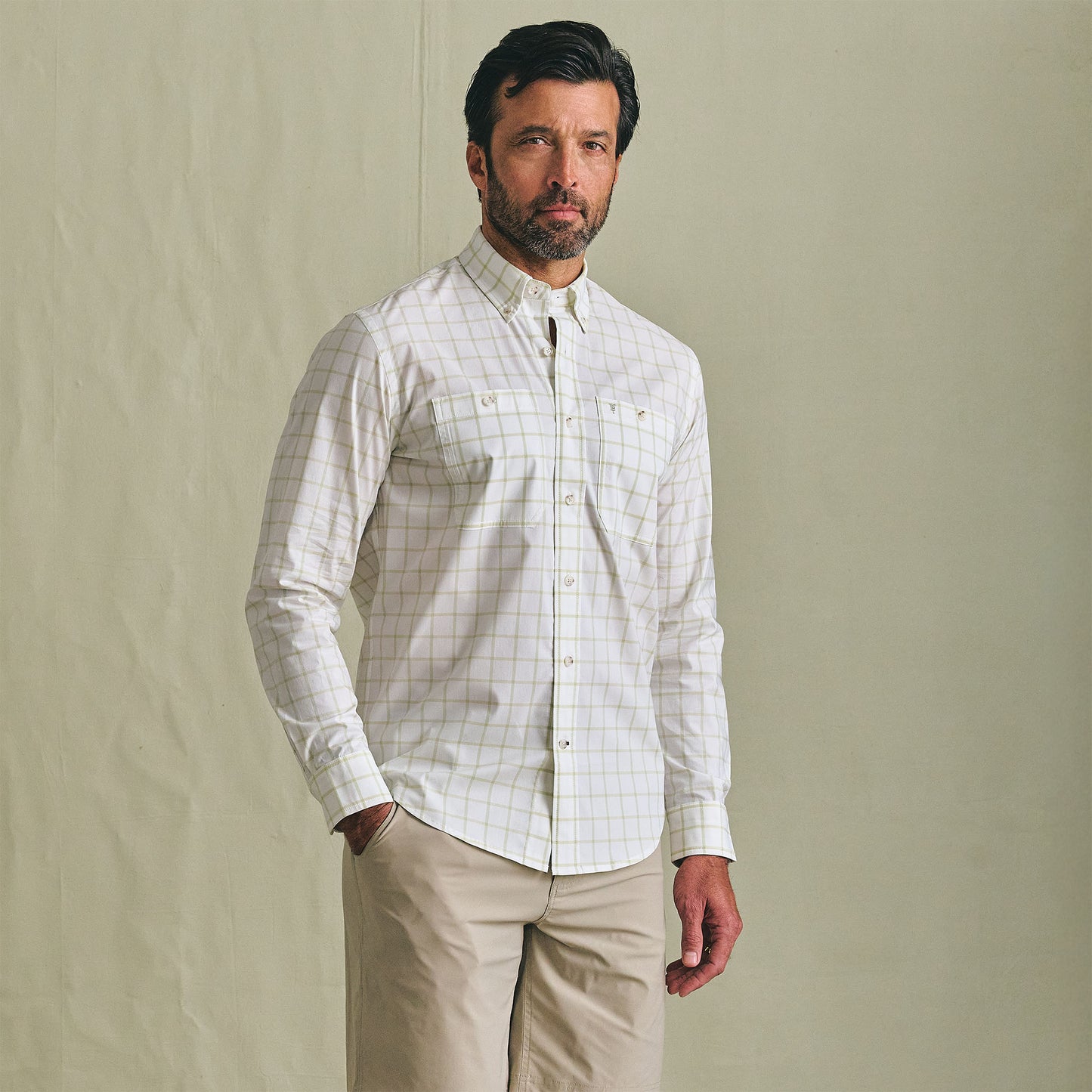 Man wears the Tom Beckbe Tidewater Shirt with khaki pants, standing in front of a plain beige background.
