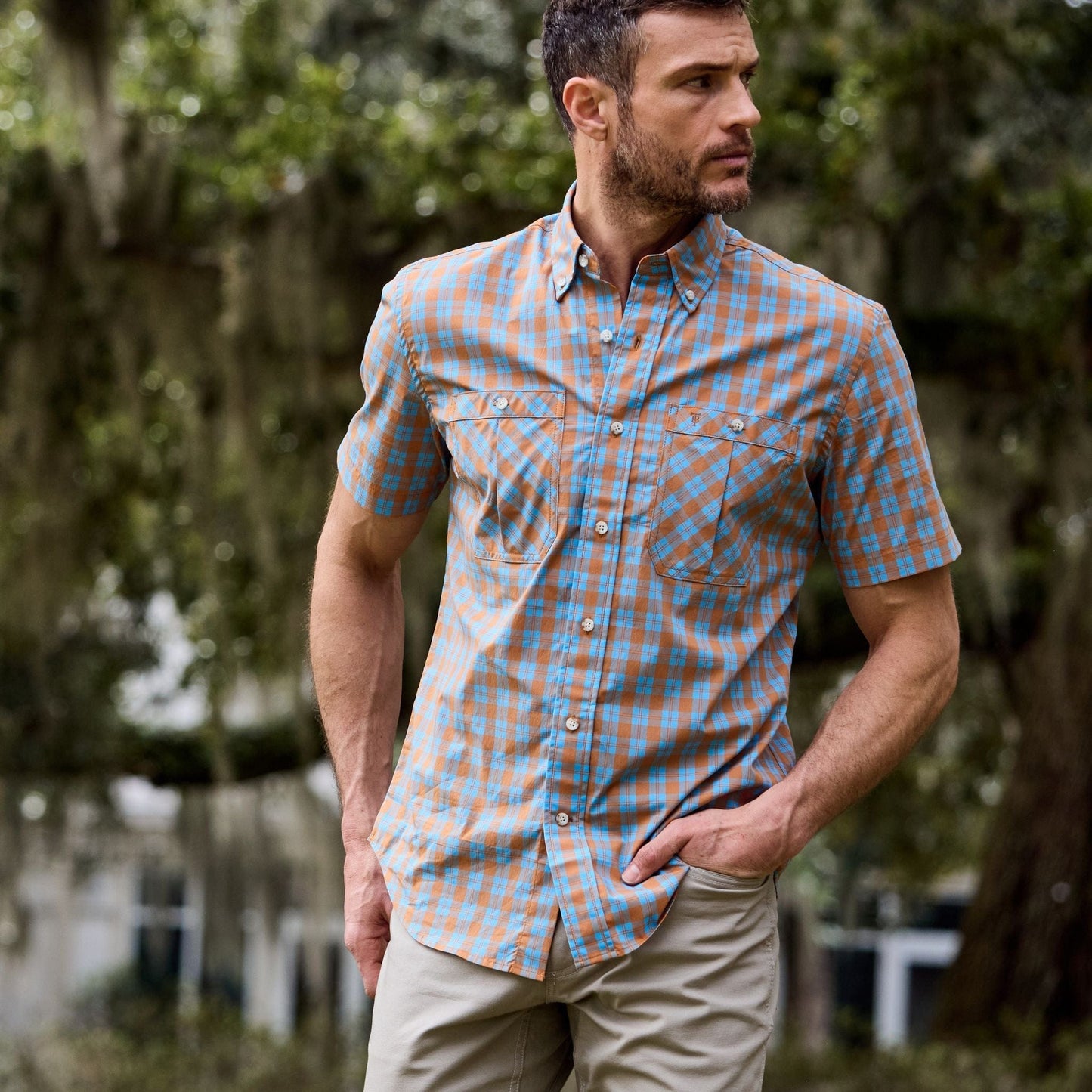 Man in Tom Beckbes Tidewater Shirt (Short Sleeve) near trees, wearing beige pants.