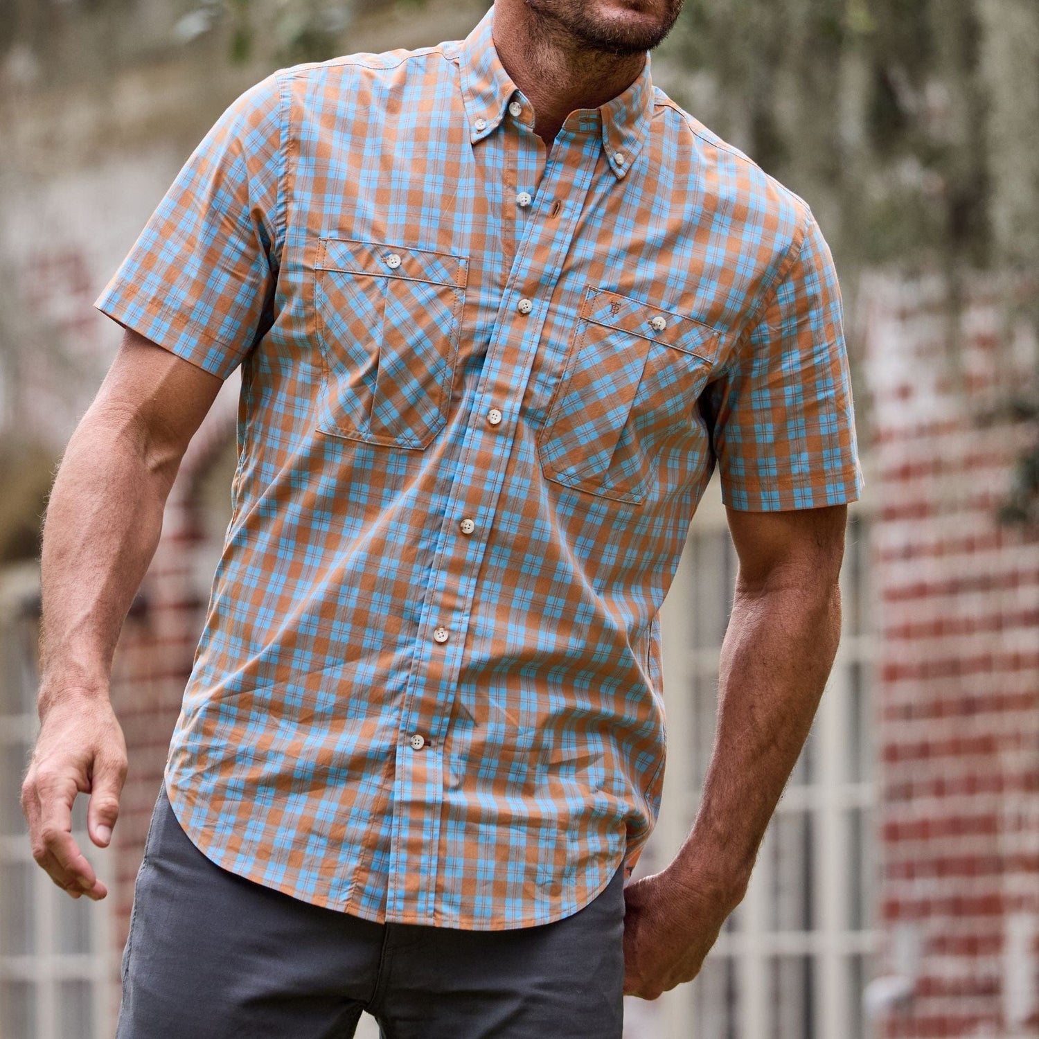 A person in a blue and orange Tidewater Shirt by Tom Beckbe stands in front of a brick building.
