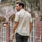 Man in Tom Beckbe Tidewater Shirt, facing away near a red brick building with large windows.