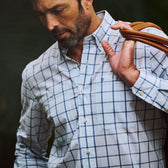 Man wearing the Tom Beckbe Tidewater Shirt, carrying a tan bag over his shoulder, looking down.
