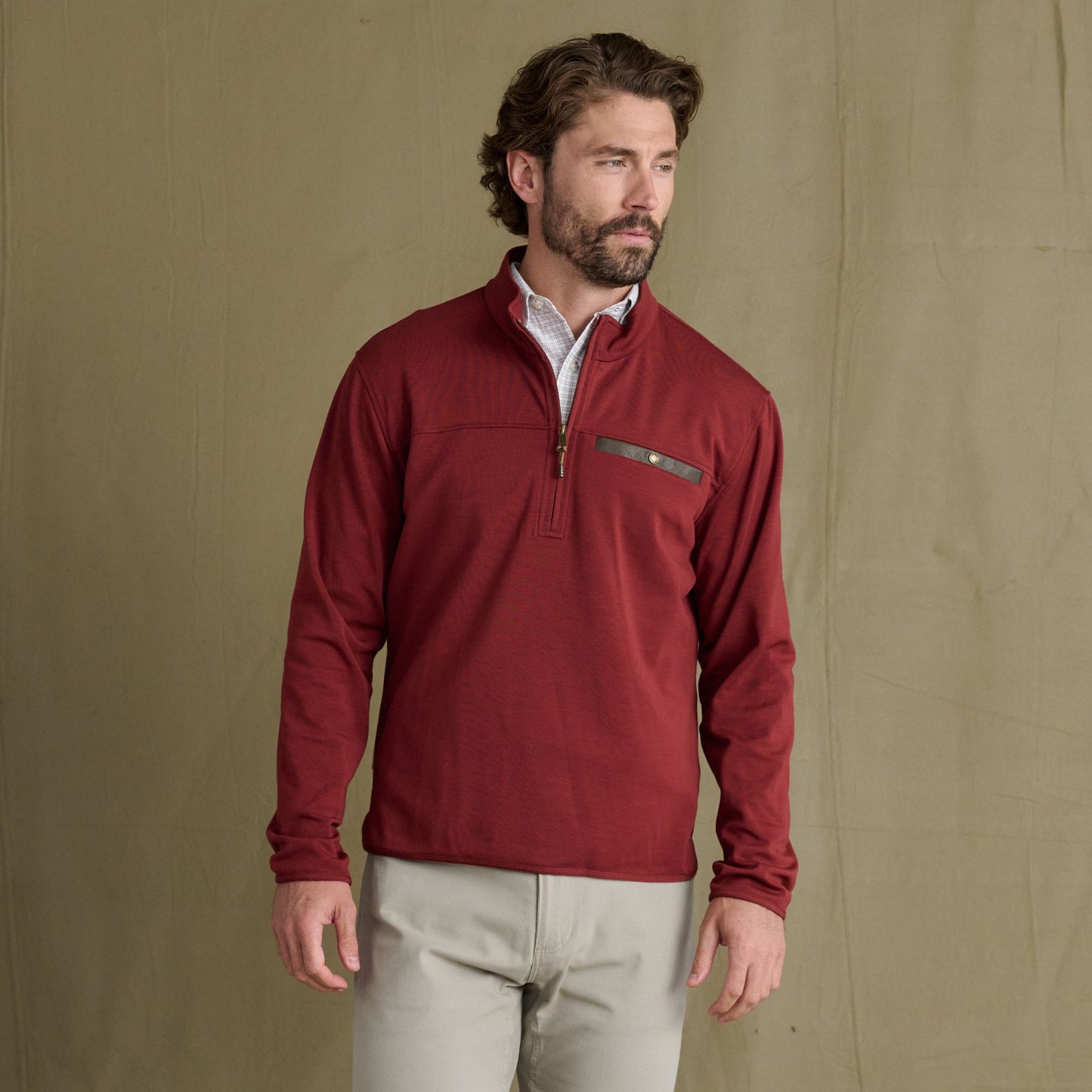 Man in a Tom Beckbe Tucker Fleece Quarter Zip and light pants stands before a plain tan backdrop.