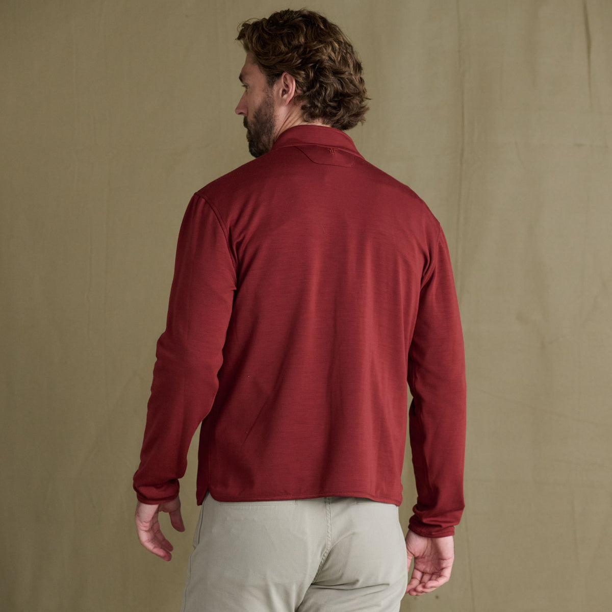 Man with light brown hair wears the Tom Beckbe Tucker Fleece Quarter Zip and beige pants, back facing the camera.