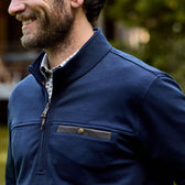 A man in a Tom Beckbe Tucker Fleece Quarter Zip, worn over a checkered shirt, stands outdoors and smiles warmly.