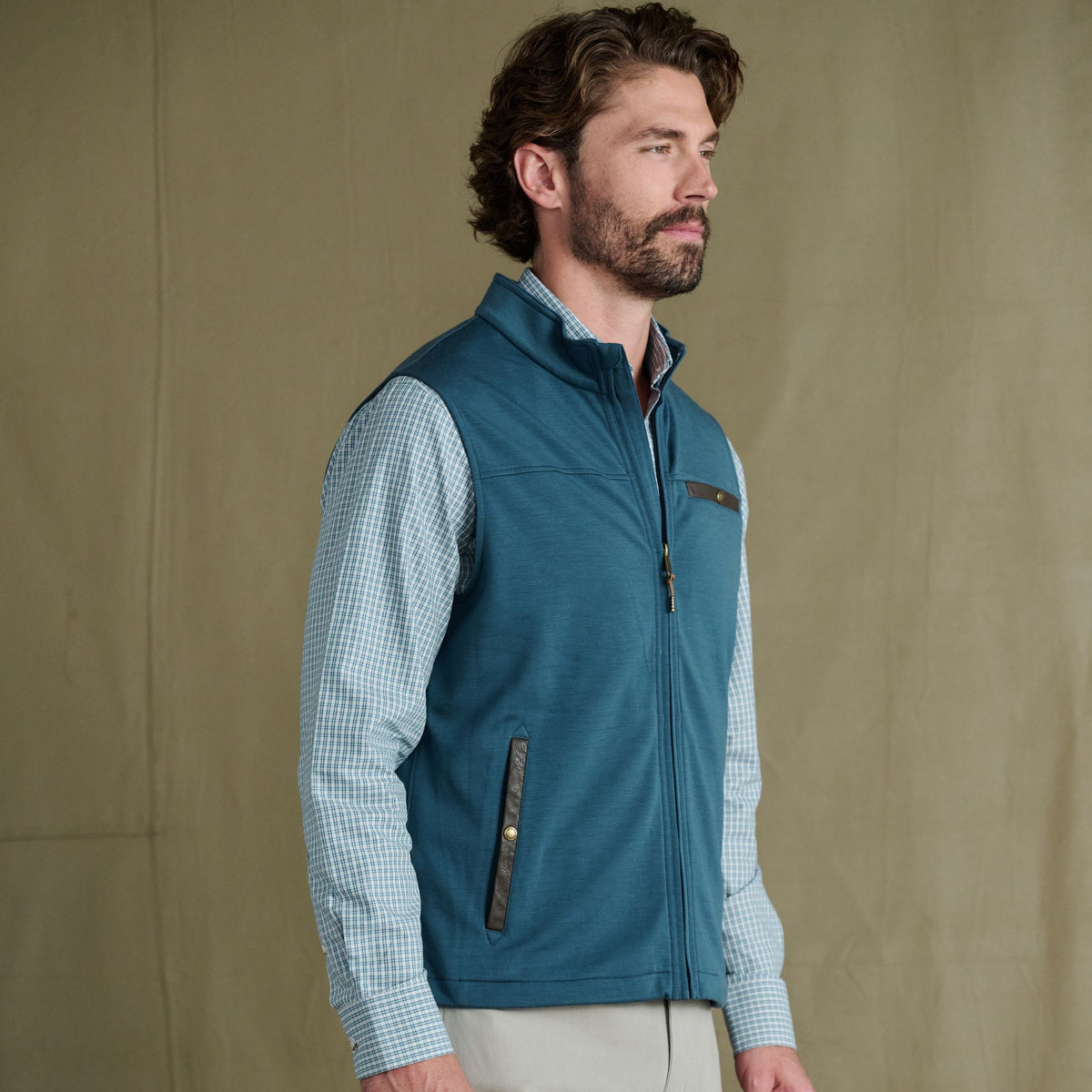Man with brown hair and beard wears the Tom Beckbe Tucker Fleece Vest over a checkered shirt, against a plain background.