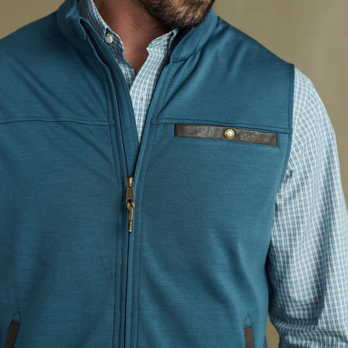 Man wearing Tom Beckbe Tucker Fleece Vest, teal zip-up over blue plaid shirt, shown neck to waist.