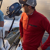 Man in a Tom Beckbe Tucker Fleece Quarter Zip stands on a boat, gazing away near another person and a motor.