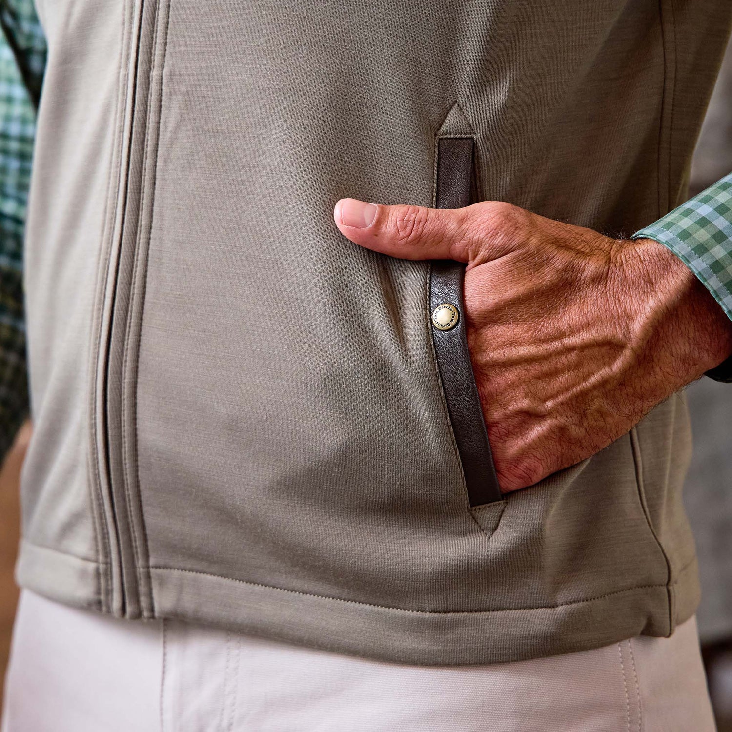 A person wearing the Tom Beckbe Tucker Fleece Vest in beige over a green checkered shirt and light pants.