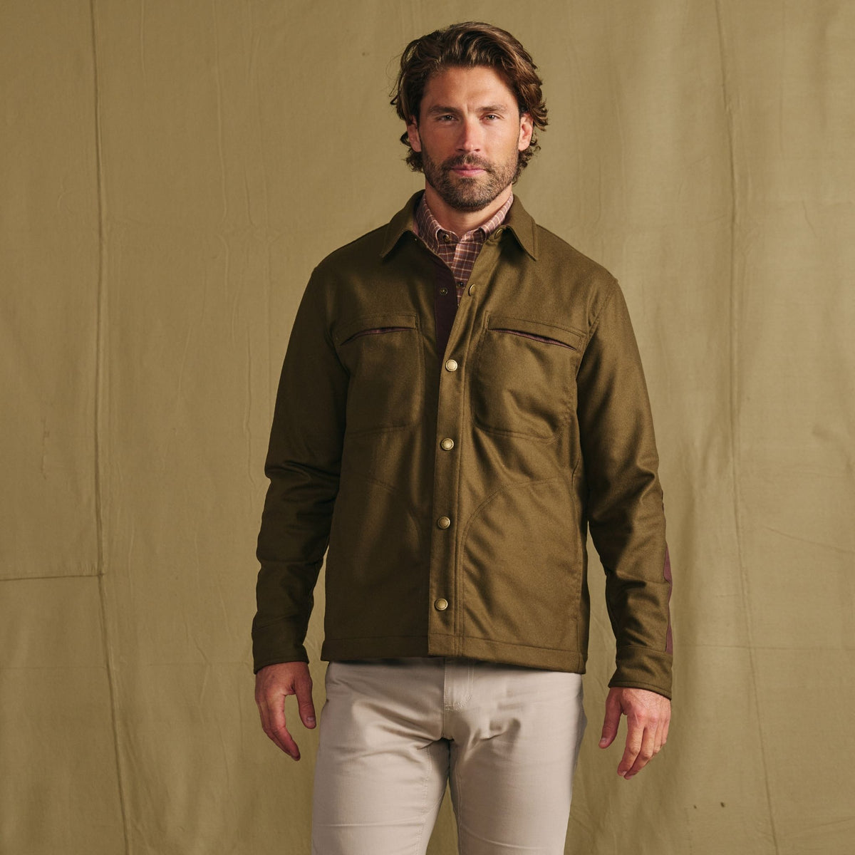 Man in Tom Beckbe Westport Wool Overshirt and light pants stands before a plain beige backdrop.