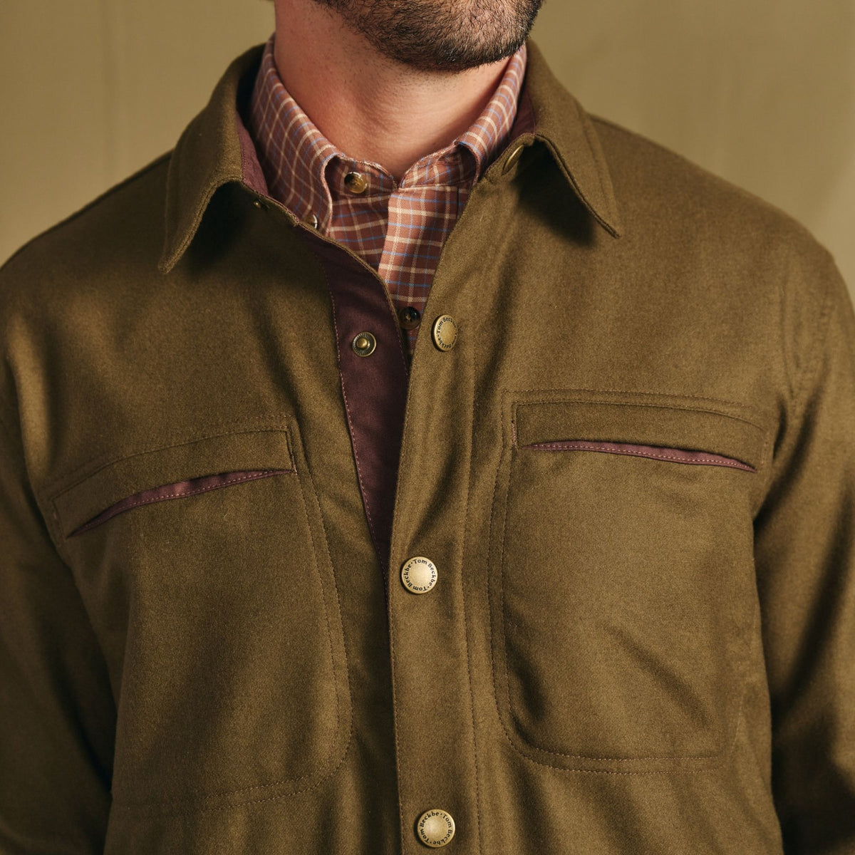 Man wears Tom Beckbe Westport Wool Overshirt in olive green over a plaid shirt, shown neck to chest.