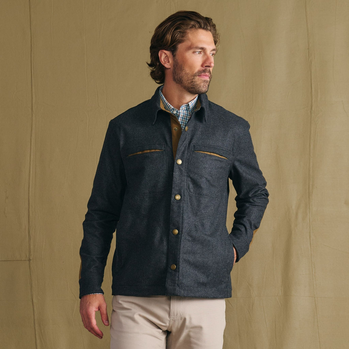 Man in Tom Beckbe Westport Wool Overshirt over a collared shirt and beige pants, against a plain tan background.