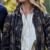 Wearing a Womens Blakeley Jacket by Tom Beckbe over a white shirt, a person strolls through blurred greenery with loose hair, capturing a casual and relaxed moment.