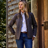 A woman in a Tom Beckbe Womens Camden Quilted Jacket stands with arms crossed, turning away against the wood siding.