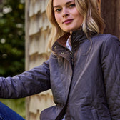 A woman in a Tom Beckbe Womens Camden Quilted Jacket sits outdoors, its windproof shell shielding her from the breeze.