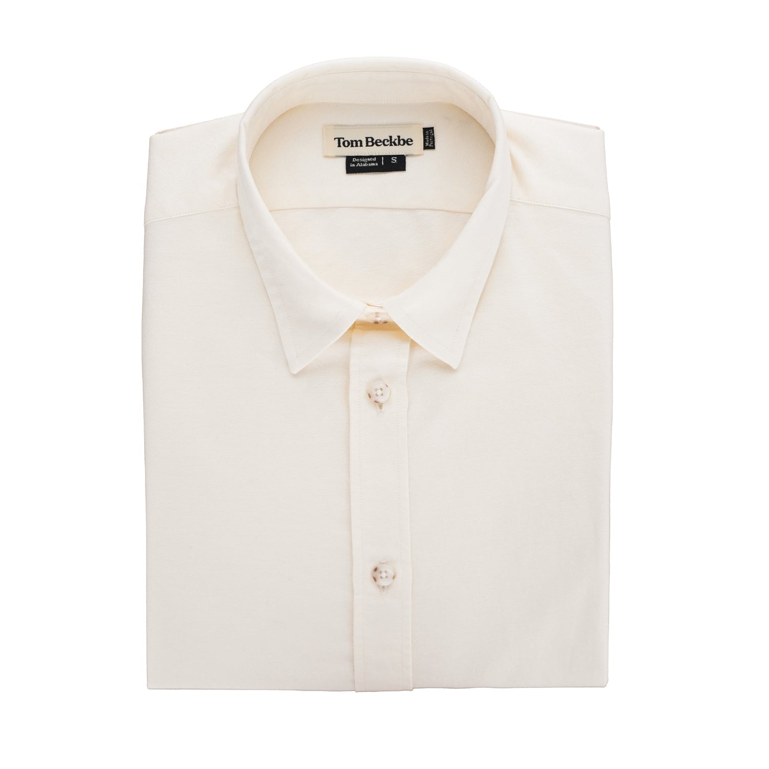 A folded beige Womens Oxford Shirt by Tom Beckbe with buttons and brand label on the collar against a plain background.