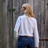 Person with blonde hair in a white Tom Beckbe Womens Oxford Shirt and jeans, standing before a wooden fence.