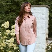 A woman in the Tom Beckbe Women's Tidewater Shirt stands outdoors near white flowers and a stone wall.
