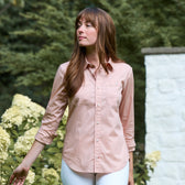 A woman wearing the Tom Beckbe Women's Tidewater Shirt and white pants stands outdoors among white flowers and greenery.