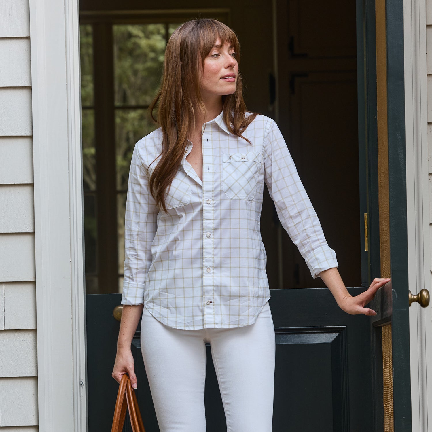 Woman wears the Tom Beckbe Women's Tidewater Shirt and white pants, standing in a doorway, holding a bag.