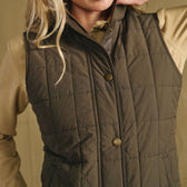 Model in Tom Beckbe Women’s Tyler Quilted Vest, olive green, over beige shirt; cropped at mouth and chin.