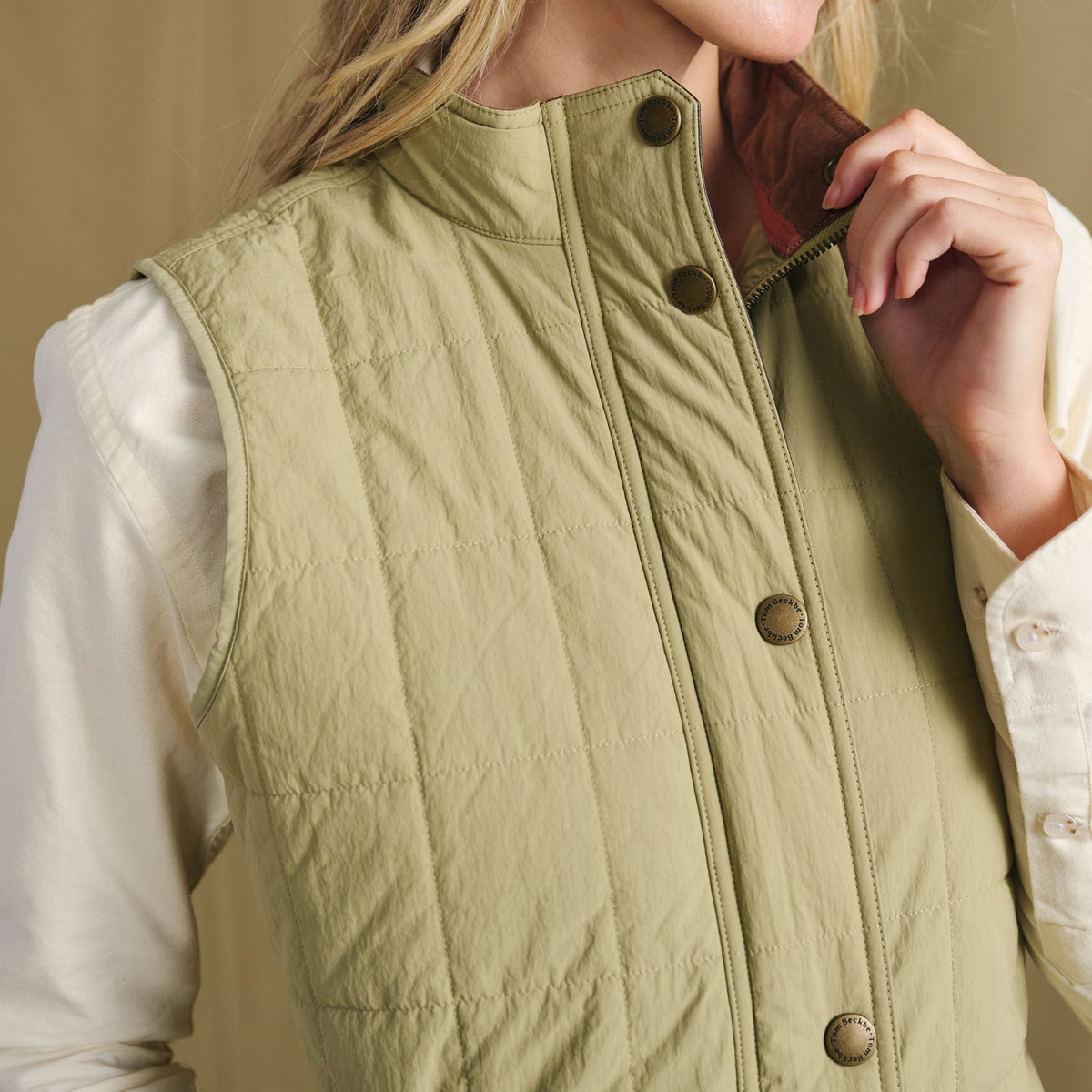 Woman adjusting the collar of a Tom Beckbe Women’s Tyler Quilted Vest over a long-sleeve white shirt.