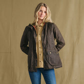Woman in Tom Beckbe’s Blakeley Jacket stands before a beige backdrop, styled with a tan shirt and blue jeans.