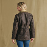 Woman in Tom Beckbe Women’s Blakeley Jacket and jeans, back to camera, against beige background.