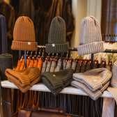Three Tom Beckbe Wool Caps in brown, green, and beige are displayed on a wooden table in-store.